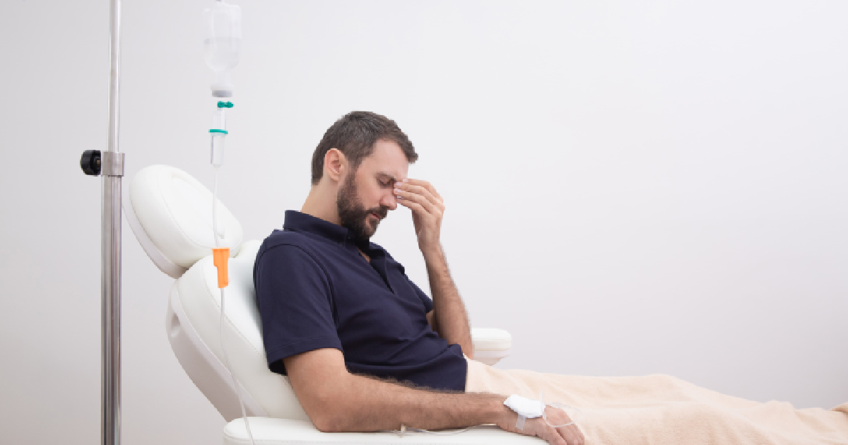 Man receiving IV therapy while experiencing a headache; seated in a medical recliner with an IV drip in his arm, suggesting hangover treatment in Torrance, CA.