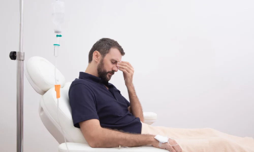 Man receiving IV therapy while experiencing a headache; seated in a medical recliner with an IV drip in his arm, suggesting hangover treatment in Torrance, CA.