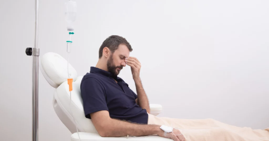 Man receiving IV therapy while experiencing a headache; seated in a medical recliner with an IV drip in his arm, suggesting hangover treatment in Torrance, CA.
